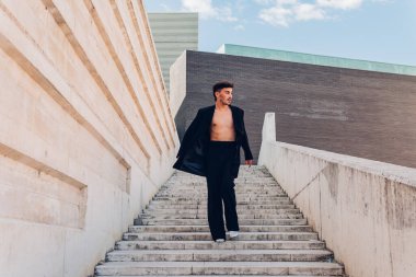 Yüzünde yapay elmaslar olan, şık siyah takım elbiseli, kentin caddesindeki merdivenlerden inen bir erkek vücudu.