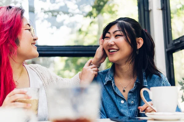 Two Asian sisters talking in a coffee shop, smiling and having fun. complicity between friends.