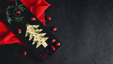 Peynirli, otlu, baharatlı ve üzümlü bir Noel ağacı solunda kırmızı bir mutfak peçetesi olan bir kesme tahtasının üzerinde sağda yazı için yeri olan siyah bir arkaplan, üstte yakın plan..