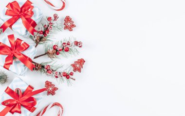 Kırmızı kurdele, şeker, köknar dalları ve ahşap Noel ağacı mandallı gri çizgili üç küçük hediye kutusu solda beyaz bir zemin üzerinde uzanıyor, sağda yazı için yer var, üstte de yakın çekim. Noel ve Yeni Yıl kavramı.
