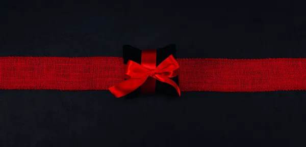 Красная Подарочная Коробка Черной Лентой Мешковатой Полосой Лежит Посередине Черном — стоковое фото