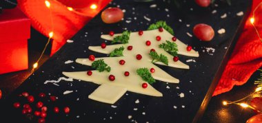 Peynirden, baharatlardan, üzümlerden ve kırmızı bir mutfak peçetesiyle kesme tahtasındaki bir çelenkten oluşan yaratıcı Noel ağacı siyah arka planda, yakın planda, köşegende yatar..