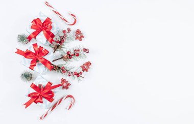 Kırmızı kurdele, şeker, köknar dalları ve ahşap Noel ağacı mandallı gri çizgili üç küçük hediye kutusu solda beyaz bir zemin üzerinde uzanıyor, sağda yazı için yer var, üstte de yakın çekim. Noel ve Yeni Yıl kavramı.