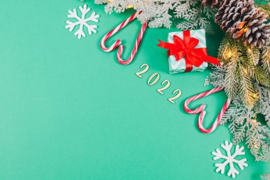 Bir hediye, iki şeker kalpli lolipop, kar tanelerini hissetti, 2022 ahşap numaralar ve sağda bir ladin dalı solda fotokopi alanı olan yeşil bir arka plan, yakın plan.