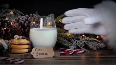 Noel Baba ahşap bir masadan bir bardak süt alır. Kurabiyeli, kozalaklı bir köknar dalı ve bir çelenk..