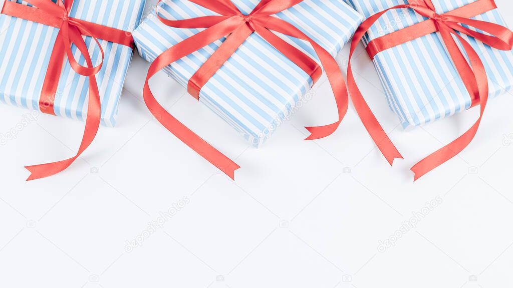 Three gift boxes in blue stripes with red ribbons lie on a white background with space for text from below, close-up top view. Christmas and New Year concept.