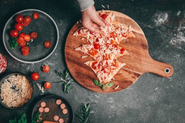 Çocuklar pizza hamurundan kesilmiş bir noel ağacına peynir serperek vişneli domatesler, sosisler ve dekorasyonla birlikte koyu bir zemin üzerinde uzanırlar. Noel ve yeni yıla hazırlık konsepti.