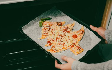 Çocuklar, fırında Noel ağacı pizzası olan bir yemek tabağı uzatıyor, yakın plan çekimde. Noel ve yeni yıla hazırlık konsepti.
