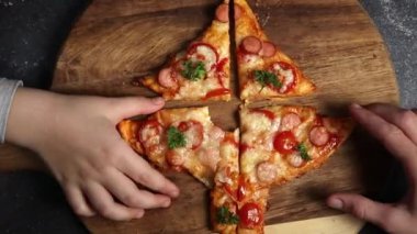 Küçük kızlar, kesilen bir Noel ağacı pizzasını karanlık bir masadaki kesme tahtasından, yakın çekim elleriyle alırlar. Aile eğlencesi ve yemek yapma konsepti.