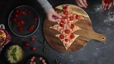 Küçük bir kız, elleri ile Noel ağacının üzerine uzanmış kiraz domatesleri üzerinde ev yapımı pizza hamuru ile koyu bir masa üzerinde kesim tahtası, yakın çekim manzarası. Aile eğlencesi ve yemek yapma konsepti.