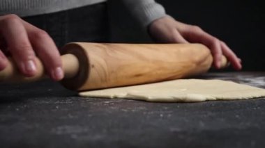 Hamur işi aşçısı bir kadın çörekler için hamur mayası ya da siyah bir masanın üzerinde tahta bir oklavanın üzerinde pizza dağıtıyor. Yan görünüm, yavaş çekim.