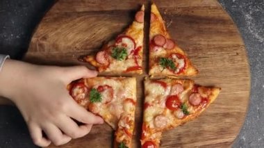 Küçük kız, elinde bir dilim pizzayı karanlık bir masadaki kesme tahtasından alıyor, yakın plan. Aile eğlencesi ve yemek yapma konsepti.