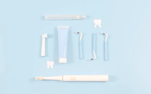 Um conjunto de pequenas escovas de dentes, pasta de dentes, uma escova de dentes elétrica e dentes de papel em azul macio. — Fotografia de Stock