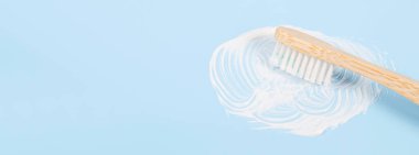 Bambu diş fırçası, sağında lekeli diş macunu, solunda fotokopi alanı olan yumuşak mavi bir arkaplan, yakın plan..
