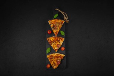 Üç dilim pizza, kiraz, fesleğen, siyah ahşap bir kesme tahtası üzerinde kırmızı çizgili bir mutfak peçetesi, siyah bir arka planda, kenarlarında fotokopi alanı, yakın plan.