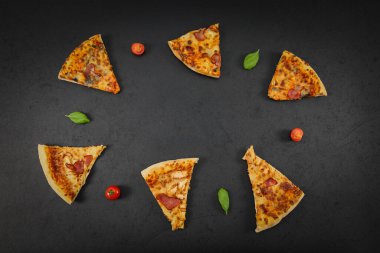 Altı dilim pizza, kiraz domatesli ve fesleğenli yaprak siyah arkaplan üzerinde düzmece bir çerçevede uzanır. Ortasında fotokopi alanı, en üstte yakın plan..