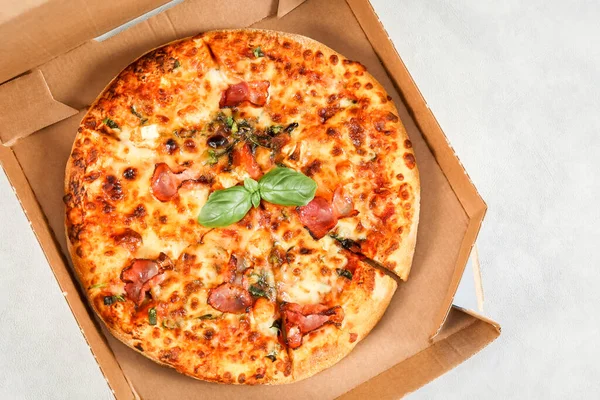 Round baked pizza in a craft box on a light gray cement background, top view close-up.