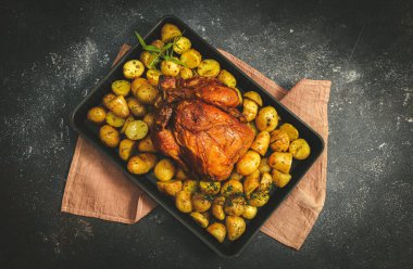 Tavuklu ve patatesli bir fırın tabağında. Altında peçete var. Arka planda koyu bir tabakta..