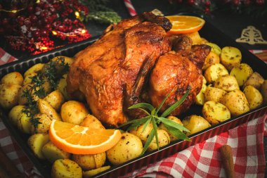 Patatesli, otlu, portakallı, tarçınlı ve şekerli lolipoplu tavuk ve siyah bir arka planda Noel süsü..