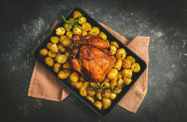 Tavuklu ve patatesli bir fırın tabağında. Altında peçete var. Arka planda koyu bir tabakta..