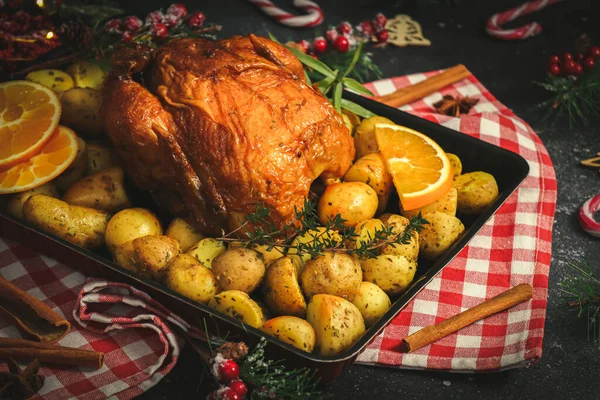 Patatesli, otlu, portakallı ve tarçınlı tavuk. Mutfakta kırmızı kareli bir peçete ve koyu arkaplanda bir noel süsü..