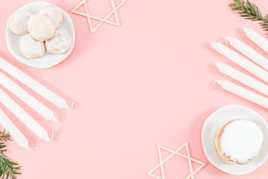 Gövde içinde toz bulunan çörekler, beyaz mumlar, köknar dalları ve David 'in tahta yıldızları pembe arka planda, merkezde fotokopi alanı, yakın plan çekimde yatıyorlar. Hanuka Kutlama Konsepti.