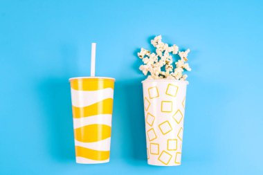 Two paper cups with yellow geometric patterns: one with popcorn and the other with a drink.