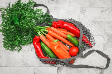 Mevsimlik sebzeler: gri bir pamuk örgüsü içinde havuç, biber ve domates mermer bir masanın üzerinde yatar, yakın plan yatar. Sağlıklı yiyecek ve çevre dostu konsept.