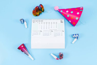 Doğum günü setiyle birlikte Mart 2022 için masaüstü kağıt takvimi: ıslıklar, borular, kağıt külahlar, renkli süsler açık mavi arkaplanda, yakın çekim üst görünümü üzerinde uzanıyor. Düz konsept takvim ve planlama.