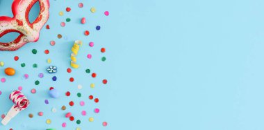 Maskeli balo maskesi, düdük, kağıt konfeti ve şekerler solda açık mavi bir zemin üzerinde uzanıyor, sağ tarafta kopya alanı, düz yakın plan. Mardi Gras bayramı konsepti.