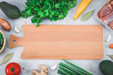 Avokado, domates, biber, taze maydanoz taze yeşil soğan, baharatlar, zencefil kökü, ahşap bir kasede donmuş ıspanak ve fotokopi alanı olan açık gri çimento arka planda boş bir kesme tahtası etrafında çiğ tavuk butları. Sağlıklı kavram 