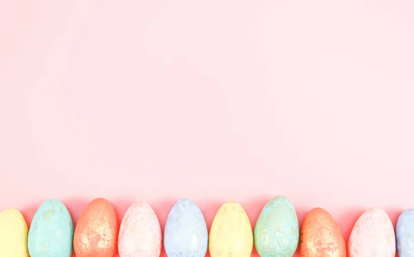 Os ovos coloridos de pastel decorativos multicores estão em uma linha de abaixo em um rosa-claro. — Fotografia de Stock