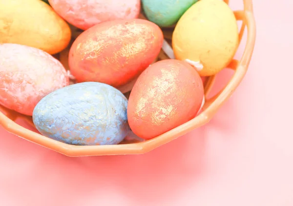 Os ovos decorativos multicores em cores pastel estão em uma cesta de plástico de vime em um rosa claro. — Fotografia de Stock