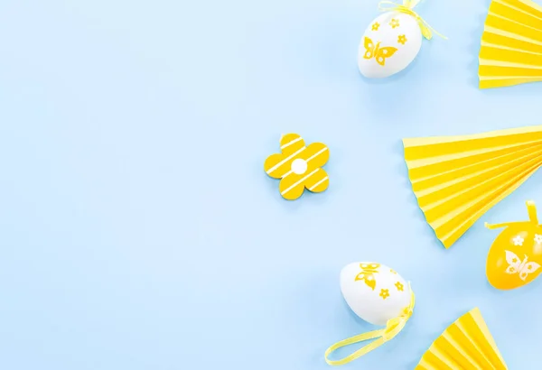 Ovos decorativos amarelos e brancos, uma flor de madeira e fãs de papel em um azul claro. — Fotografia de Stock