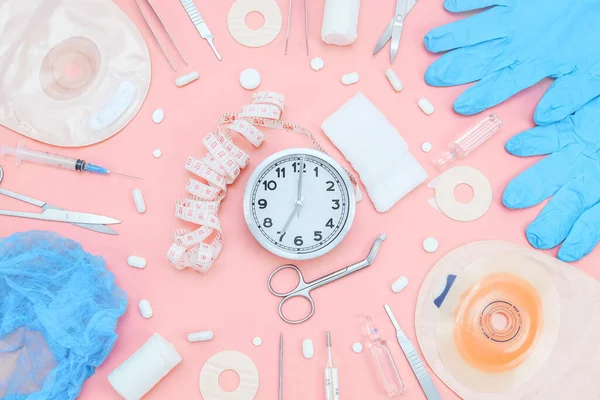 Хирургический набор для операции с часами и мешком для колостомии на мягком розовом фоне. — стоковое фото