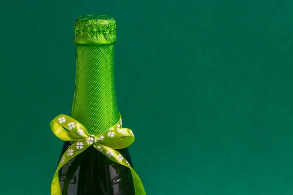 One bottle of green beer with a ribbon tied in a bow on the left on a green . — Stock Photo, Image