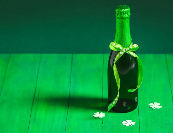 Egy üveg zöld sör masnival és három papír lóherével egy zöldön.. — Stock Fotó