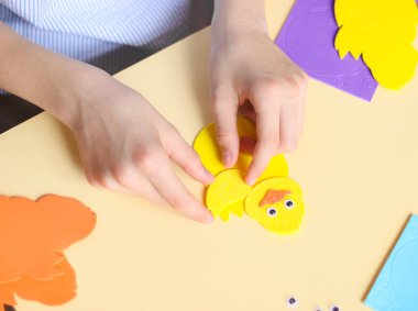 Kafkasyalı genç bir kızın elleri parmaklarıyla sarı bir tavuğa kanat çıkartması yapıştırıyor.