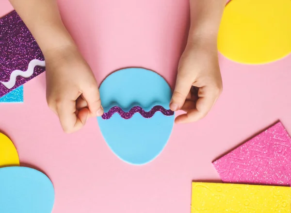 The hands of a little caucasian girl glue a lilac zigzag sticker on a felt egg — Foto Stock