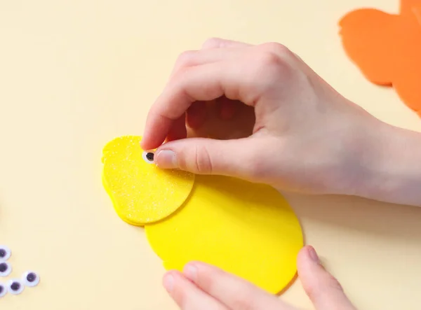 The hand of a caucasian teenage girl glues a decorative eye on a felt yellow chick — Foto Stock