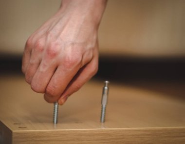 Kafkasyalı genç bir adamın elleri, parmaklarıyla yatağın ahşap kısmında bir cıvata bükerek, odasında yerde oturuyor, yakın görüş açısında. Mobilya montajı, alışveriş anlayışı, evde