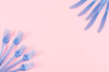 Beş mavi plastik şeffaf bıçak ve beş çatal üzerinde pembe bir arka planda duruyor. Ortadaki metnin için fotokopi alanı var. Yakın plan. Ekoloji konsepti, plastik çöp, tek kullanımlık