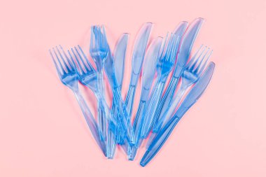 Plastik şeffaf bıçaklar ve çatallar pembe arka planda, düz bir yakın plan üzerinde yatıyorlar. Ekoloji konsepti, plastik çöp, tek kullanımlık plastik sofra takımı, poster, ekoloji bayrağı, ekoloji günü.