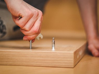 Kafkasyalı genç bir adamın elleri, parmaklarıyla yatağın ahşap kısmında bir cıvata bükerek, odasında yerde oturuyor, yakın görüş açısında. Mobilya montajı, alışveriş anlayışı, evde