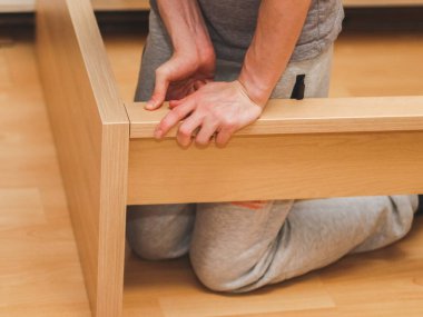 Kafkas kökenli genç bir adam elleriyle tahta bir tahta ile yatak başlığını birbirine bağlıyor parmaklarıyla bastırıyor, odasında yerde oturuyor, yakından bakıyor. Birleştirme kavramı