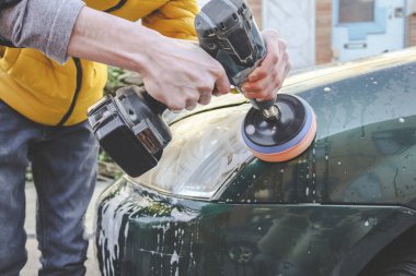 Kafkasyalı genç bir adamın elleri, süngerli bir matkapla matkabı deliyor ve arabasının farını deterjan sabunuyla parlatıyor. Yakın plan, araba yıkama ve araba farlarıyla temizlik kavramı..