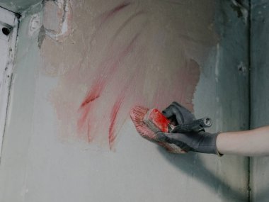 Genç beyaz bir alçıcının inşaat eldivenindeki bir el büyük bir fırça tutar ve kirli bir duvara çürük, yakın görüş için kırmızı sertleştirici harç uygular. Dairelerin ve evlerin yenilenmesi, duvarların sıvalanması.,