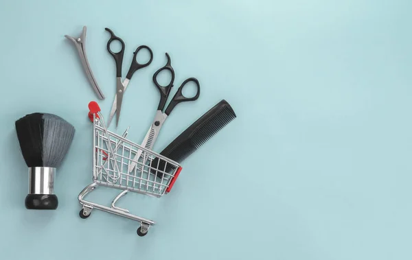 Scissors, comb and other hairdressing accessories lie in a mini cart on the left on a blue background with copy space on the right, flatlay close-up. The concept of hairdressers and shops.