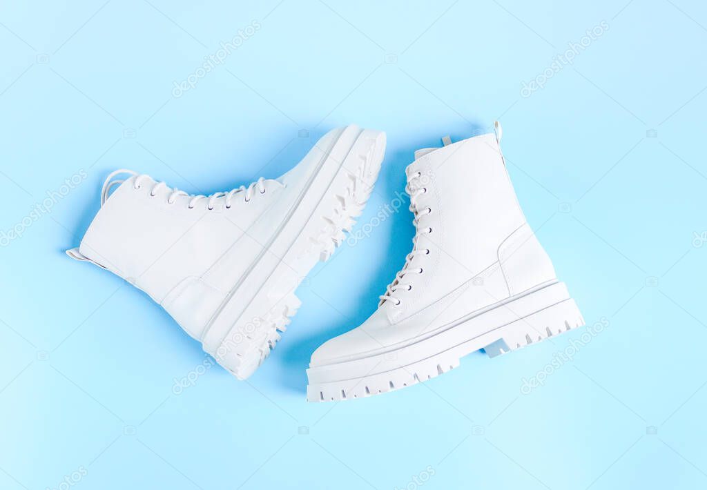 White demi-season martens boots made of eco-leather with a rough sole lie in the center on a light blue background, flat lay close-up. The concept of women's shoes.
