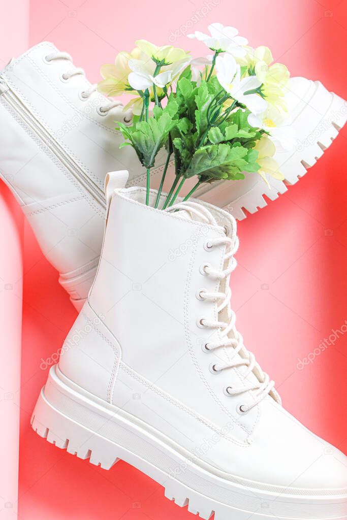 White demi-season martens boots made of eco-leather with a rough sole with a bouquet of spring flowers on a pink background, flat lay close-up. The concept of women's shoes.